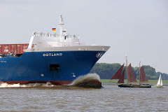 Cargo Ship GOTLAND in voller Fahrt auf der Elbe; der Wulstbug den Wasserwiderstand. Im Hintergrund ein historischer Kutter / Ewer mit braunen Segeln und ein Sportsegelboot.