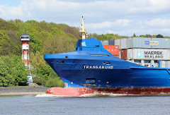 Das Frachtschiff TRANSANUND auf der Elbe vor Hamburg Wittenberge - im Hintergrund das Leuchtfeuer am Ufer der Elbe. Die 2007 gebaute TRANSANUND hat eine Länge von knapp 142m und kann 801 TEU Container transportieren.