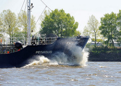 Der 62m lange und 10m breite Tanker Pegasus fährt auf der Elbe vor dem Hamburger Bubendey Ufer; hoch spritz die Gischt am Bug des Tankschiffs