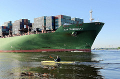 Bug des Frachters XIN SHANGHAI auf der Elbe bei Hamburg - ein Paddelboot fährt stromaufwärts.