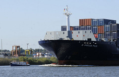 Der Frachter X PRESS FUJI läuft in den Hamburger Hafen ein - eine kleine Barkasse der Hamburger Hafenrundfährt fährt vor dem Bug des Schiffs.
