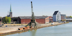 Blick auf den Dortmund-Ems-Kanal in Münster - Hafenkran am Kanalufer; im Hintergrund Gebäude am Münsteraner Hafen und der Kirchturm der Hl. Kreuzkirche.
