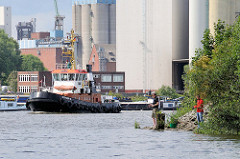 Schlepper auf dem Reiherstieg in Hamburg Wilhelmsburg - im Hintergrund Silo-Anlagen, Angler am Ufer.
