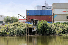 Alter Kran am Ufer des Schmidtkanals in Hamburg Wilhelmsburg; dahinter Containerstapel.