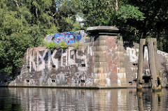 Reste eines Brückenfundaments am Tiefstackkanal in Hamburg Rothenburgsort / Billbrook, die Mauern sind mit Graffiti bemalt; re. ein alter Holzdalben zum Festmachen von Schiffen.
