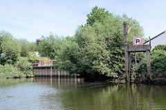 Spundwand - Hochwasserschutzanlage bei der historischen Schleuse vom Schmidtkanal in Hamburg Wilhelmsburg; re. eine alte Verladestelle auf Betonstelzen mit Handkran.