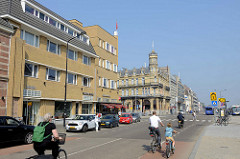 Blick in die Stationsstraat  von Maastricht; im Hintergrund die historische Architektur vom Amrâth Grand Hotel de l'Empereuram Hauptbahnhof der Stadt - im Vordergrund  ein Wohnhaus / Geschäftshaus mit gelber Ziegelfassade.