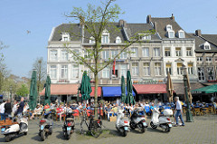 Mehrstöckige Wohn- und Geschäftshäuser am Markt von Maastricht; Restaurants und Cafés haben Tische und Stühle Straße gestellt - die Plätze sind dicht besetzt, die Gäste sitzen in der Sonne.