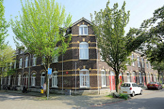 Eckgebäude, einstöckiger  Wohnblock - geschlossene  Straßenbebauung mit roter Backsteinfassade und gelben  Zierbändern in der Van Den Berghstraat in Maastricht.