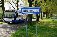 Straßenschild / Ortsschild von Roermond,  ein Bus Richtung Venlo fährt vorbei.