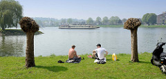 Picknick am Ufer der Maas in Maastricht - ein Fahrgastschiff / Ausflugsschiff fährt flussabwärts.