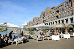 Promenade am Stadthafen von Venlo, lang gezogene mehrstöckige Wohnhäuser - Gastronomie mit Holzbänken und Sonnenschirmen am Wasser.