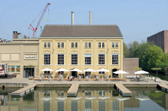 Blick vom Maasboulevard über das Bassin in Maastricht; ein altes Hafengebäude ist das restauriert und wird als Restaurant und Kino  genutzt.