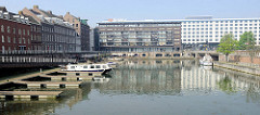 Altes Hafenbecken  / Bassin am Maasboulevard in Maastricht. Bootsstege und Motorboote liegen in der Marina - im Hintergrund neugebaute Wohnhäuser mit Balkon und die Fabrikgebäude der ehemaligen  Keramikfabrik Sphinx.
