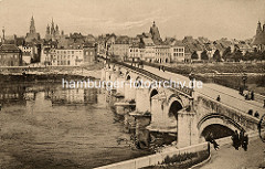 Historisches Panorama der Stadt Maastricht in den Niederlanden; Kirchtürme über den Dächern der Stadt; und Passanten schlendern über die Steinbrücke.
