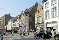 Wohnhäuser mit Geschäften im Erdgeschoss - unterschiedliche Architekturformen in der Grote Gracht von Maastricht; Radfahrerinnen fahren auf der Straße, Fußgänger überqueren einen Fußgängerüberweg.