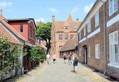 Wohnhäuser mit blühenden Rosen an der Hauswand - Puggaardsgade in Ribe; im Hintergrund der alte Bischofspalast Taarnborg. Das Renaissancegebäude wurde 1580 erbaut und wird jetzt u. a. als Ausbildungszentrum genutzt.