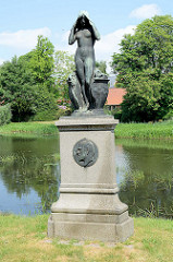 Grünanlage in Ribe - Bronzeskulptur; nackte Frau, die aus einem zerbrochenen Krug steigt.