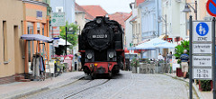Die Bäderbahn Molli fährt durch die Fussgängerzone / Straße Molli in Bad Doberan. Der Zug wird von der Dampflok 992322-8 gezogen.