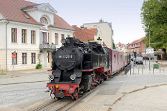 Die Bäderbahn Molli mit der Dampflok  992322-8 am Alexandrinenplatz in Bad Doberan - im Hintergrund das Haus Gottesfrieden des Stadtarchitekten Carl Theodor Sverin, das im klassizistischen Baustil 1824 errichtet wurde.