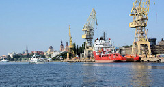 Blick von der Westoder auf die Hafenanlagen von Stettin - Frachtschiffe und Kräne; im Hintergrund die historischen Türme der alten Hansestadt.