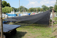 Im Fischereihafen  von Ziegenort /  Trzebież  sind Fischernetze zum Trocknen aufgehängt; im Hintergrund im Hintergrund liegen Sportboote in der Marina des Dorfes an der Oder bei Stettin.