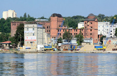 Leerstehendes Backsteingebäude am Hafen von Stettin; Kaianlage mit Kran und Schüttgut.
