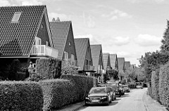 Einfamilienhäuser / Einzelhäuser mit Satteldach in der Gartenstadt von Hamburg Alsterdorf. Frisch geschnittene Hecken Grenzen die Grundstücke ab, Autos parken vor den Häusern.