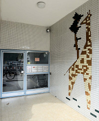 Eingangsdekoration eines Wohnhauses in Hamburg Lurup; Baustil der 1960er Jahre,  Kachelmosaik - Giraffe mit Baum.