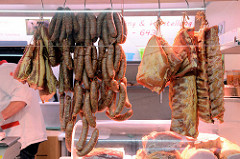 Marktstand einer Schlachterrei auf dem Wochenmarkt im Hamburger Stadtteil Hamm; Würste, Rippenstücke und Schwarten hängen an einem Haken.
