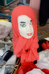 Marktstand mit Mützen und Tüchern auf dem  Wochenmarkt in der Großen Bergstraße, Stadtteil Hamburg Altona / Altstadt;  ein Styroporkopf mit auf gemalten Augen und rotem Mund trägt ein rotes Kopftuch.