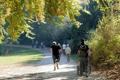 Herbst in der Hansestadt Hamburg, Besucherinnen der Grünanlage am Weiher in Eimsbüttel joggen  oder gehen unter den Herbstbäumen spazieren.