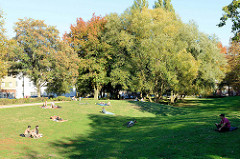 Liegewiese  in der Grünanlage Göhlbachtal im Hamburger Stadtteil Harburg. Parkbesucherinnen liegen auf Decken in der herbstlichen Abendsonne.