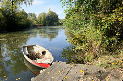 Bootsteg mit rotem Ruderboot an der Hövelpromenade der Dove Elbe im Hamburger Stadtteil Wilhelmsburg.