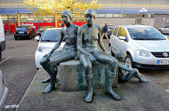 Kunst im öffentlichen Raum; Bronzeskulptur zwei Frauen mit Kind, Steinblock zwischen Autos auf dem Parkplatz Bei den Höfen in Hamburg Jenfeld.