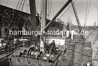 Historische Fotografien aus dem Hamburger Fotoarchiv. Blick über das Deck eines Frachtschiffs im Segelschiffhafen - ein Arbeiter steht an der elektrischen Winde, die den Ladebaum des Schiffs betreibt.