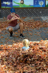 Herbst in der Marktpassage von Hamburg Neugraben, ein Kind spielt im Herbstlaub.