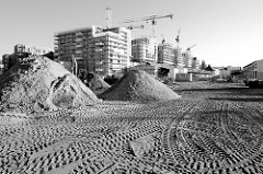 Baustelle mit großen Sandhaufen und Reifenspuren auf dem Gelände des ehemaligen Güterbahnhofs Hamburg Altona - im Hintergrund entstehen Wohngebäude.
