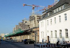 Historische Lagerhäuser mit Laderampe  auf dem Gelände des ehemaligen Güterbahnhofs Hamburg Altona Nord, dahinter die Baustelle von Neubauwohnungen und Baukräne.
