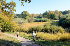 Fußweg am Ufer der Flottbeck im Naturschutzgebiet Flottbeck-Tal im Jensichpark von Hamburg-Othmarschen; Bäume und Gräser zeigen ihre herbstliche Färbung.