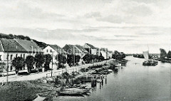 Historische Ansicht vom Ufer der Alten Oder in der Stadt Oderberg; Holzkähne sind an Land gezogen, zwei Binnenschiffe fahren mit Segelunterstützung oderabwärts.