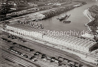 Luftfoto vom Windhukkai des Süd-West-Hafens,  dem Lagerschuppen 59  mit den Tonnengewölben am Veddeler 9amm und den Gleisanlagen des Güterbahnhofs Hamburg Süd. Ein Frachter liegt an den Dalben in der Mitte des Hafenbeckens.