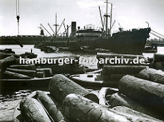 Ein Frachtschiff liegt im Südwesthafen auf Reede; seine Ladung, die in Säcken verpackt ist wird gelöscht und mit bordeigenem Ladegeschirr auf Schuten verladen - im Hintergrund die Lagergebäude am Windhukkai.