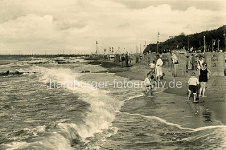 Historisches Foto vom Ostseestrand in Brunshaupten / Kühlungsborn; Kinder spielen in den Wellen der Ostsee - Strandkörbe sind aufgestellt die Touristen stehen  in Straßenanzug oder Badekleidung in Sand.