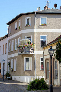 Zweistöckiges Gebäude mit Rauputz, Balkon mit Sonnenschirm prächtig blühenden Pflanzen in Oderberg.