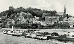 Altes Bild von Oderberg an der Alten Oder, ein Schlepper mit hohem Schornstein unter Dampf und ein Lastkahn liegen am Kai, auf  dem Holz gestapelt ist. An Land die Häuser der Stadt, rechts die Nikolaikirche - in der Bildmitte Hotel/Gaststätte go