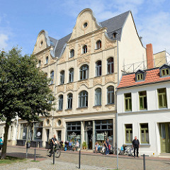 Wohn- und Geschäftshaus mit aufwändig dekorierte Jugendstilfassade in der Straße Hinter dem Chor in Wismar; Café mit Tischen auf dem Gehsteig in der Sonne.
