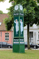 Alte Normaluhr mit der Reklame für das Waschmittel Persil; weiß gekleidete Frau mit Hut hält eine Packung in der Hand; Wiese am Lindgengarten in der Hansestadt Wismar.
