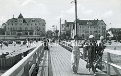 Historische Ansicht der  Seebrücke im Ostseebad Arendsee / Kühlungsborn; Hotels an der Strandpromenade - Liegestühle am Strand, Touristen in Badekleidung / Bademantel auf der Holzbrücke.