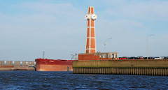 Pegelturm mit leerstehendem Flachgebäude an der Einfahrt zum Segelschiffhafen in Hamburg; auf der anderen Seite der Elbe liegt ein Frachtschiff am Kirchenpauerkai.